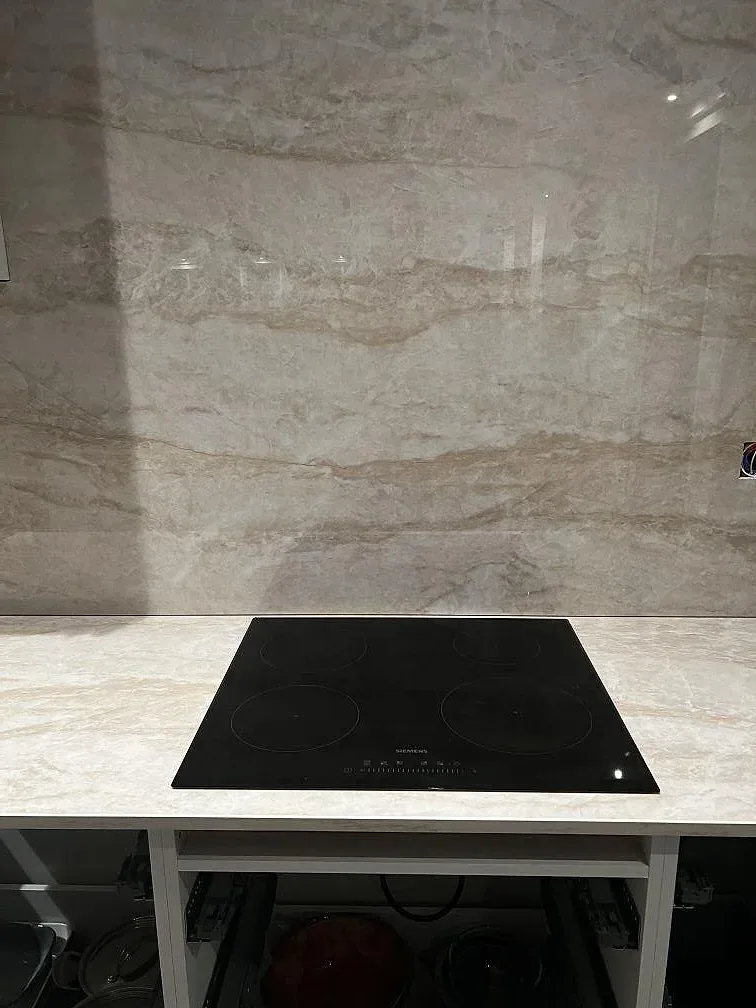Svart häll i polerad Dekton Arga med matchande väggbeklädnad och öppna köksstommar under montering i Stenkullen.