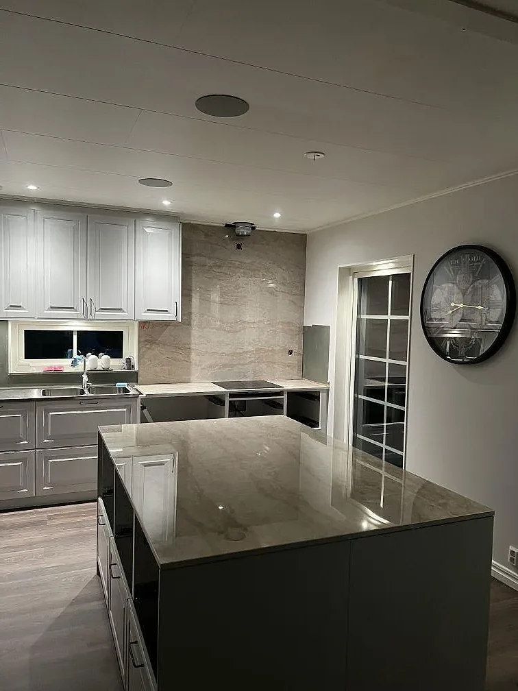 Köksbänkskiva i polerad Dekton Arga keramik med halvö, underlimmad rostfri diskho och svart häll i ett kök i Stenkullen.