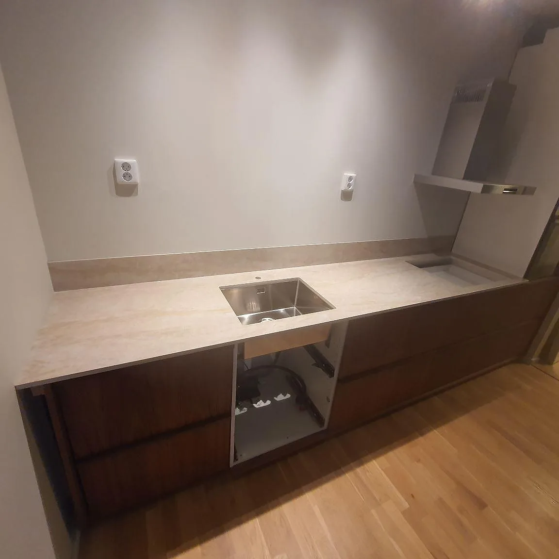 Köksbänkskiva i Dekton Arga, polerad keramik i ljus krämton med mjuk ådring, med underlimmad rostfri diskho och låg stänkkant i ett kök i Stockholm.