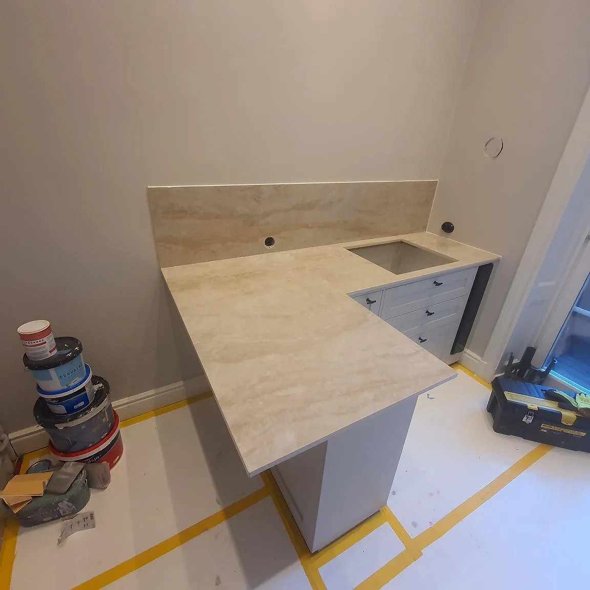 L-format köksbänkskiva i krämvit Dekton Arga keramik med köksö och mjuk ådring, monterad i ett kök under installation i Stockholm.