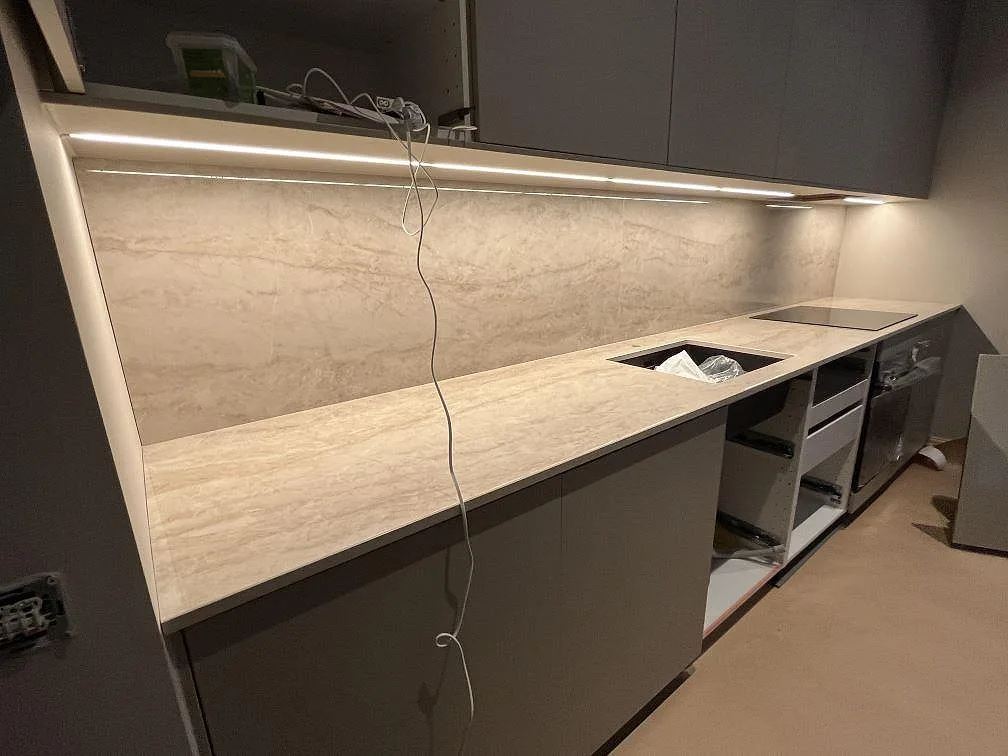 Köksbänkskiva i polerad Dekton Arga med matchande stänkskydd, diskhoöppning och hällplats i ett grått kök i Stockholm.