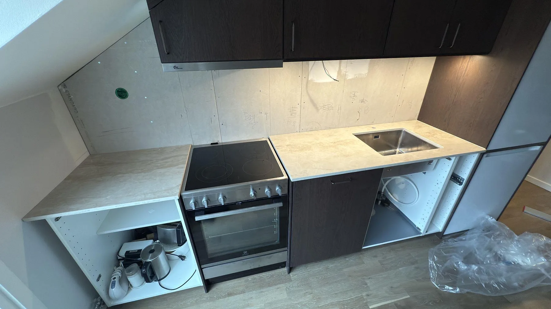 Köksbänkskiva i ljus Dekton Arga, polerad keramik, med underlimmad rostfri diskho och plats för fristående spis i ett kök under montering i Stockholm.