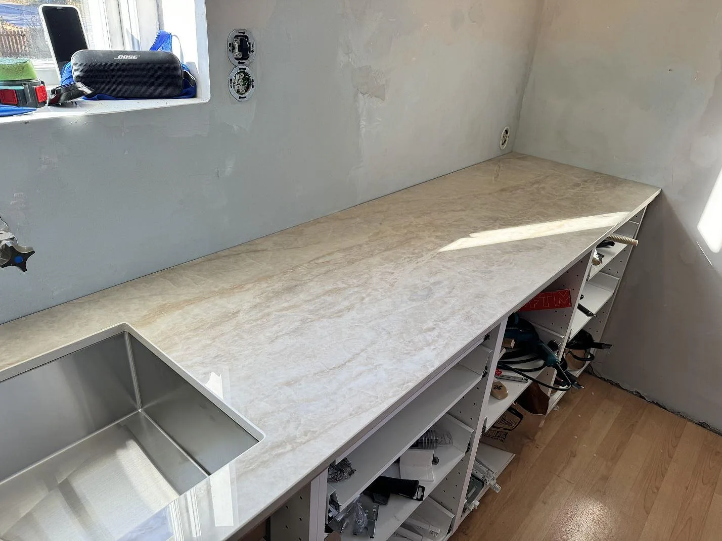 Lång köksbänkskiva i polerad Dekton Arga, 20 mm, med rostfri diskho och synlig ådring under montering i Svedala.