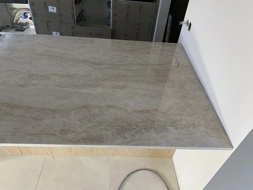 Polerad köksö i ljusgrå, marmorlik Dekton Arga keramik med tydlig ådring i ett kök i Tibro, fotograferad uppifrån under montering.