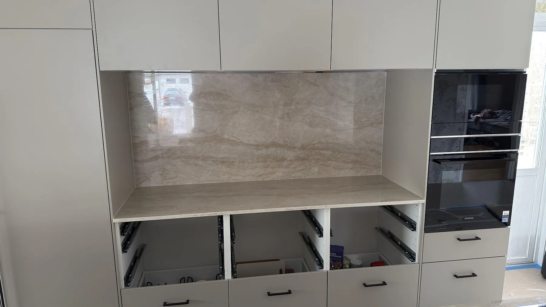 Heltäckande polerat stänkskydd i Dekton Arga ovanför bänkskivan längs bakre väggen i ett kök i Torsby, fotograferat under montering.