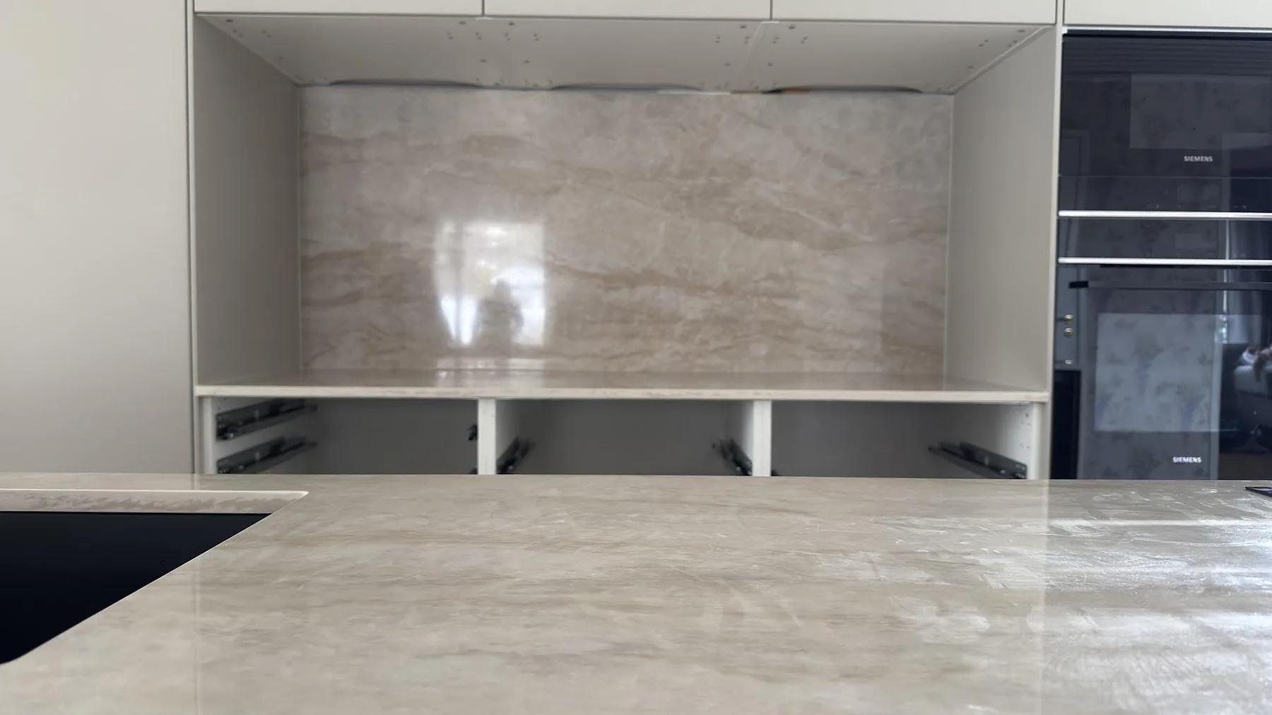 Närbild på den polerade köksön och stänkskyddet i Dekton Arga i ett kök i Torsby, krämbeige keramik med mjuk ådring.