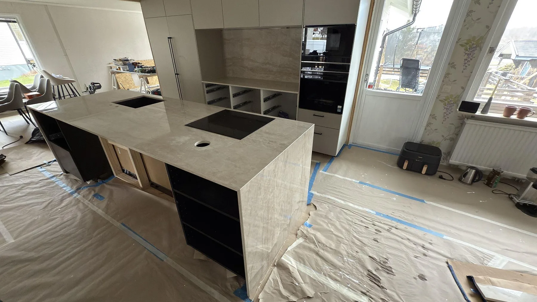 Köksö i Dekton Arga sedd i helhet med köksrummet i Torsby, polerad keramikbänkskiva med vattenfallskant under montering.