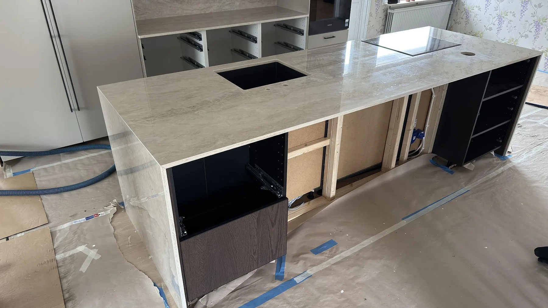 Köksö i Dekton Arga, polerad keramik i krämbeige med brungyllene ådring, med förberedda urtag för häll och diskho i ett kök under montering i Torsby.