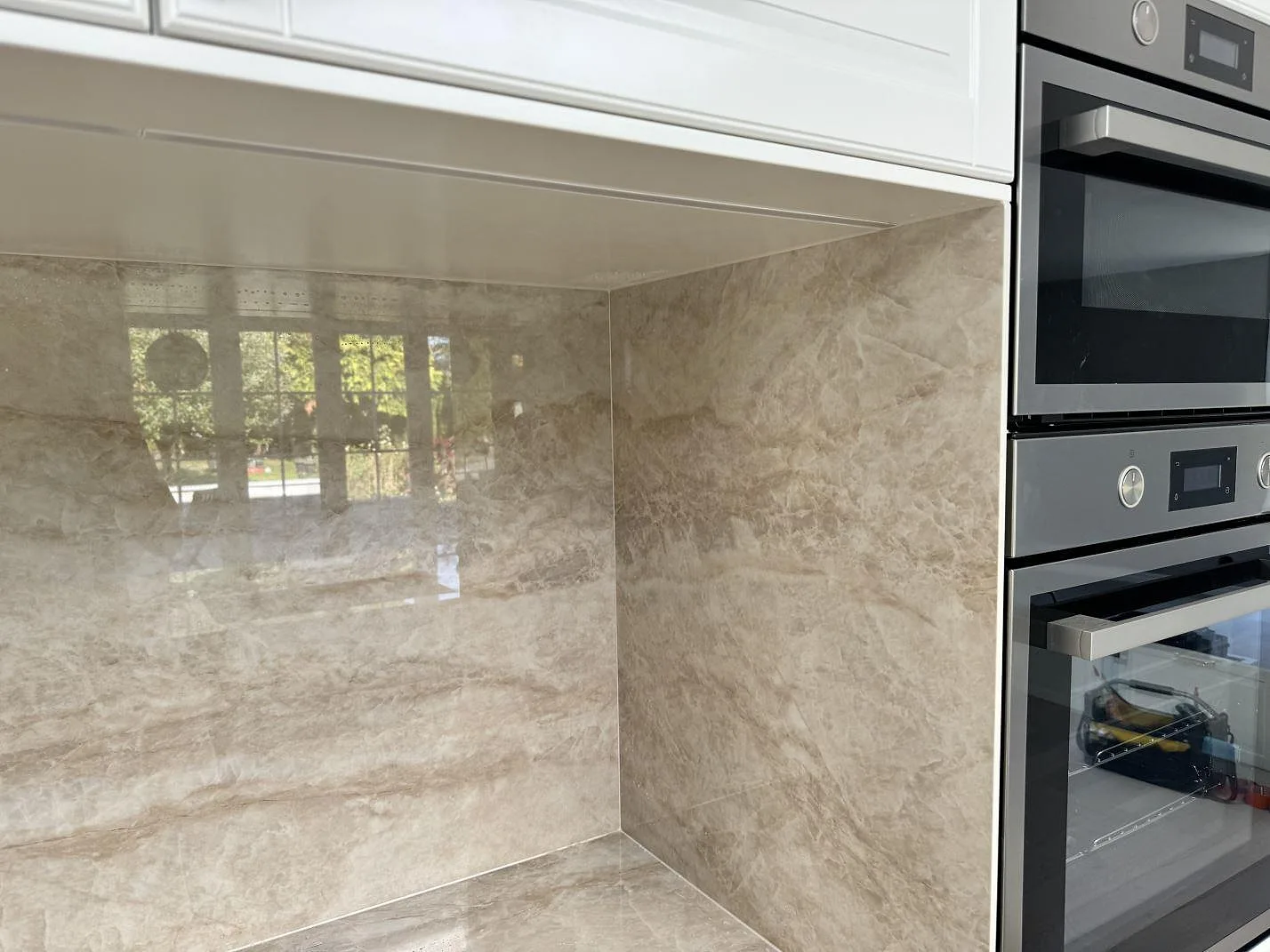 Väggbeklädnad i polerad Dekton Arga, keramik, runt arbetsyta och inbyggnadsugn i ett kök i Tygelsjö.