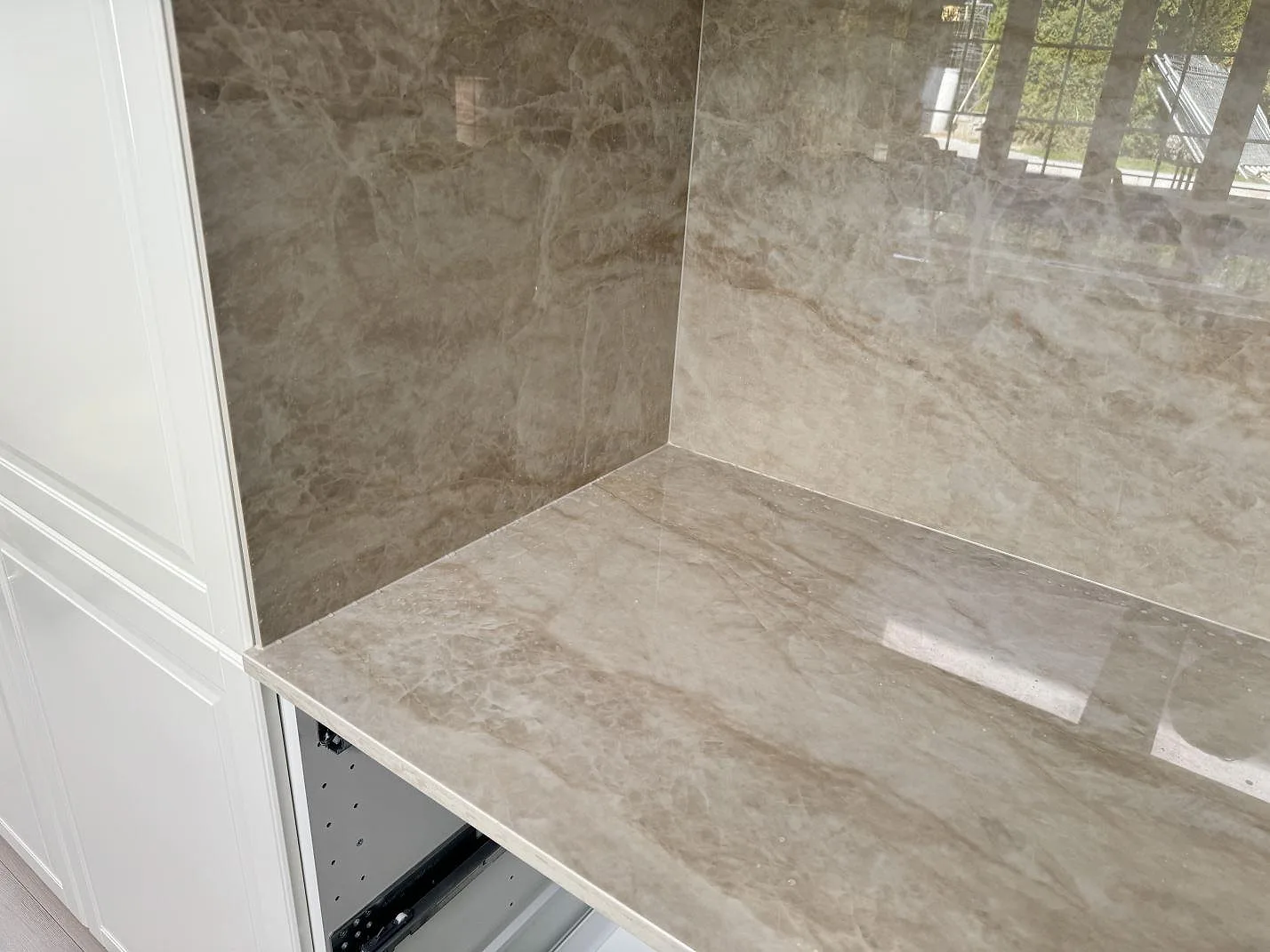 Hörnvy av polerad Dekton Arga, keramik, som bänkskiva och väggpanel i köket i Tygelsjö.