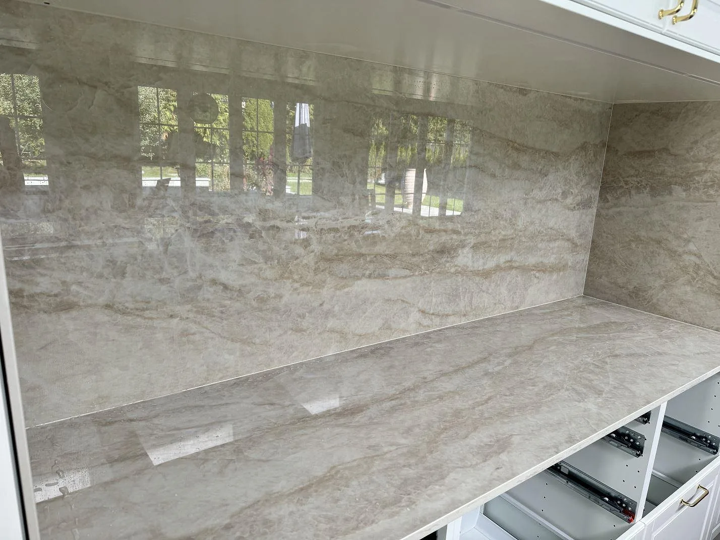 Sammanhängande bänkskiva och väggbeklädnad i polerad Dekton Arga, keramik, i ett vitt kök i Tygelsjö.