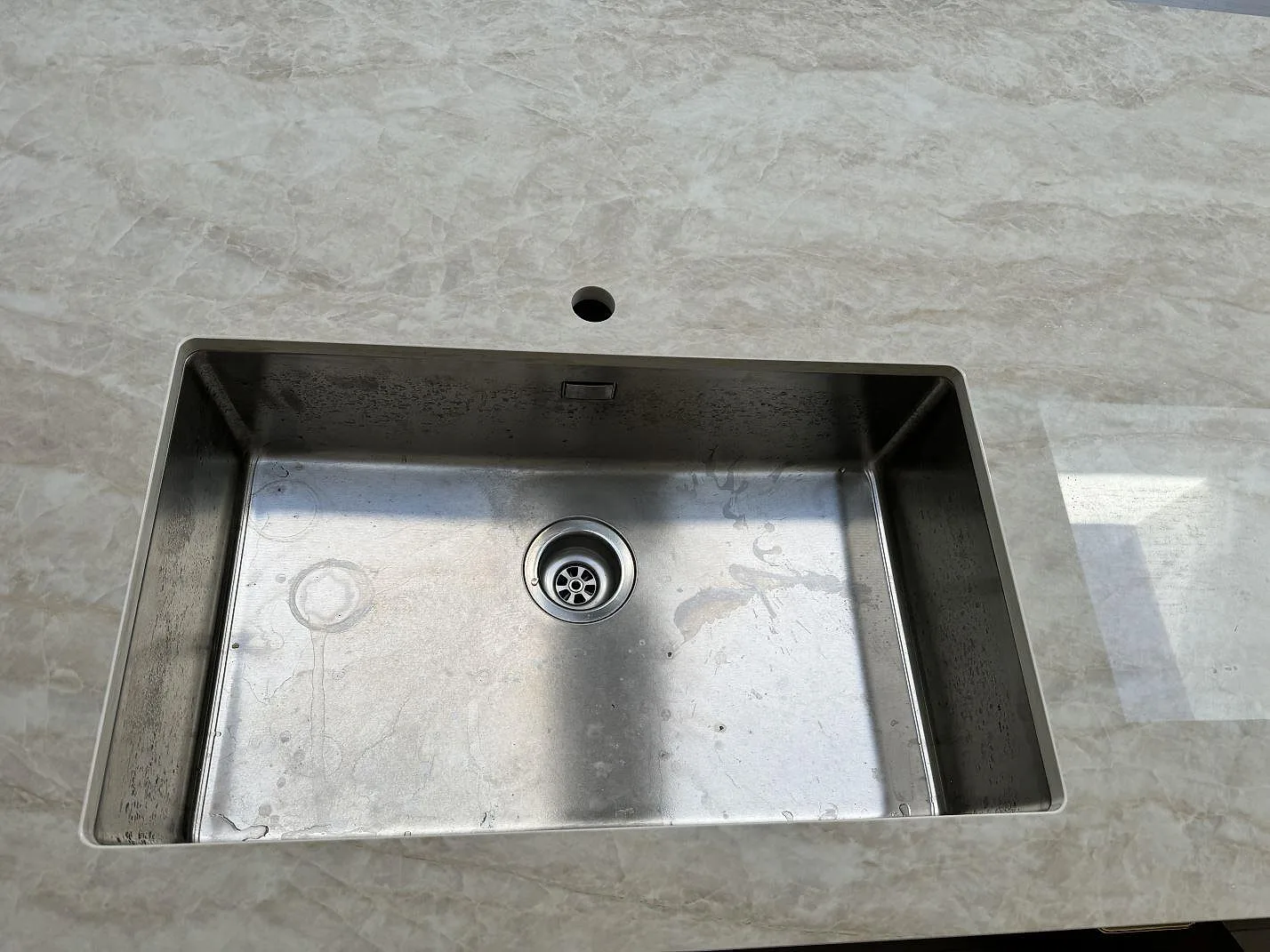 Närbild på rostfri diskho i polerad Dekton Arga, keramik, med blandarhål i köksbänken i Tygelsjö.