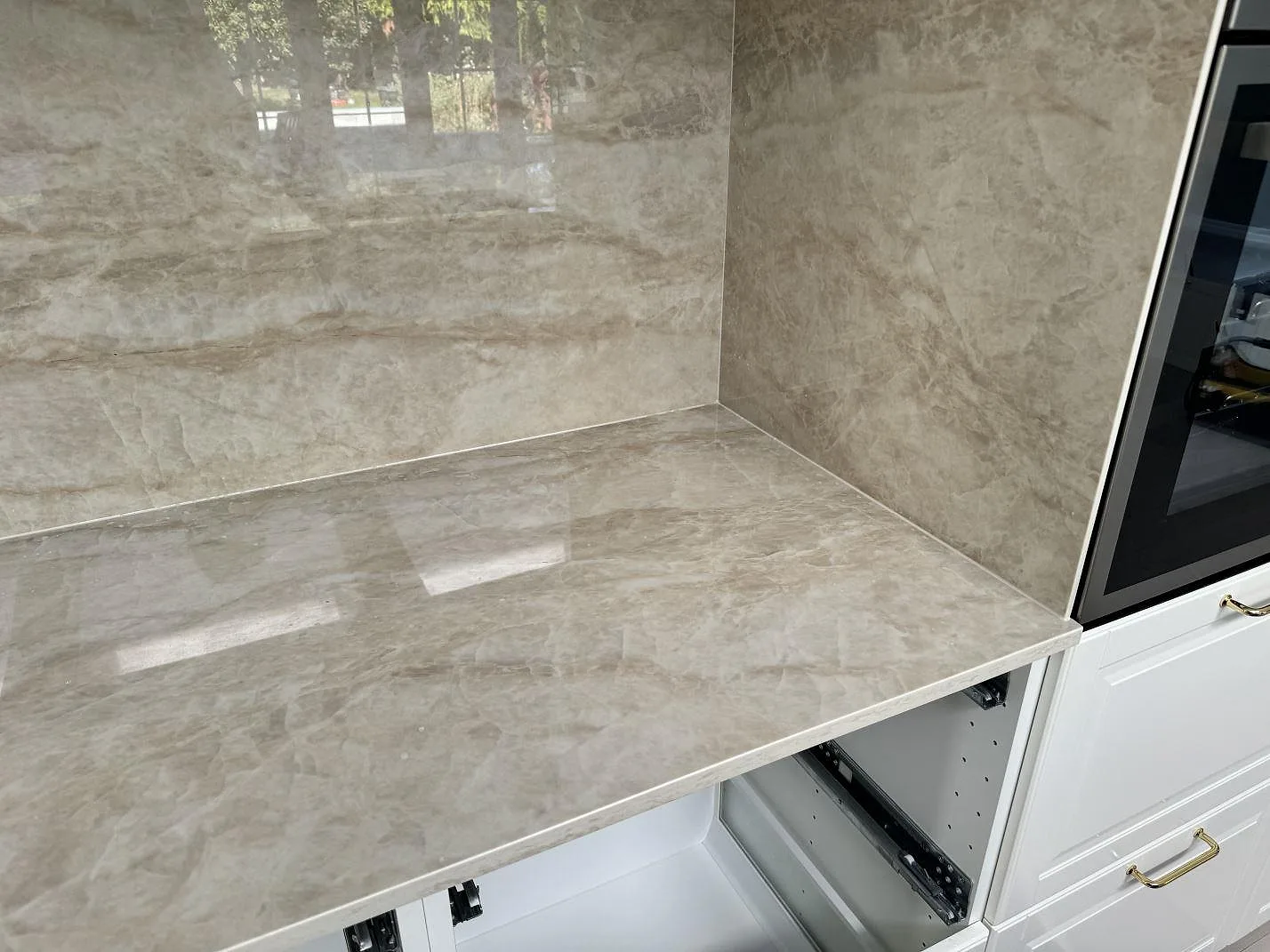 Polerad Dekton Arga som köksbänkskiva och väggbeklädnad i keramik vid högskåp i ett kök i Tygelsjö.