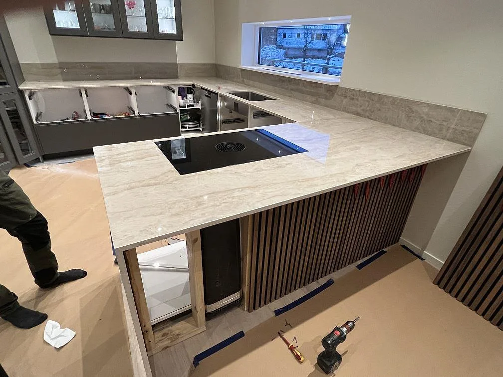 Polerad köksbänkskiva i beige Dekton Arga keramik med svart häll och uppvikt stänkskydd i ett kök i Tyresö.