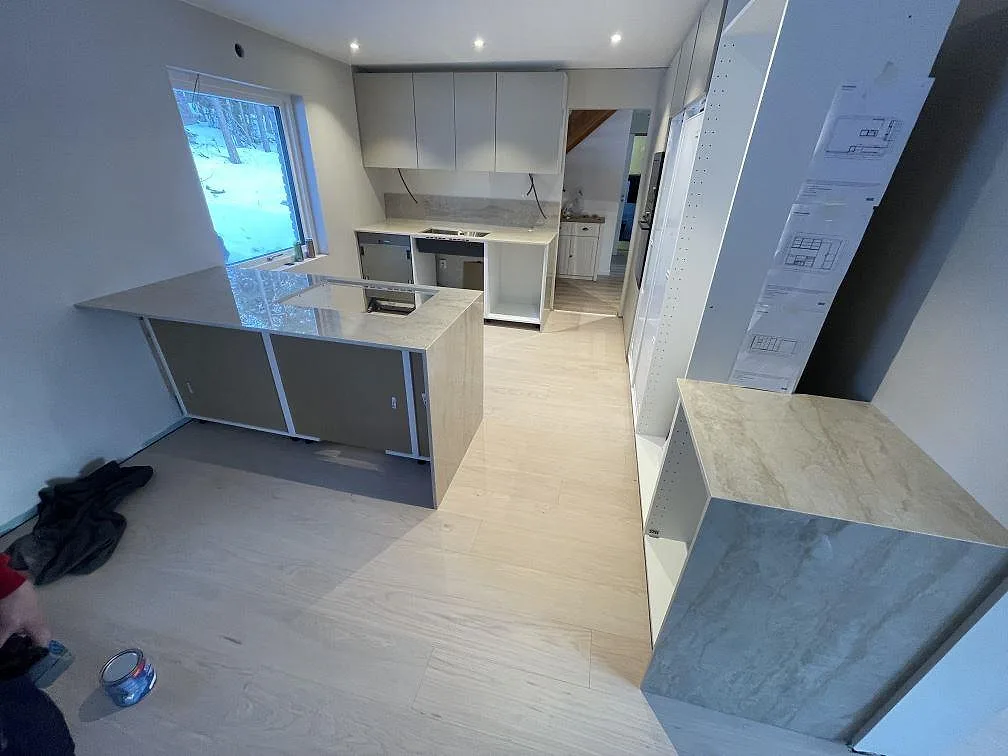Köksbänkskiva och köksö i ljus Dekton Arga, polerad, med urtag för induktionshäll och bänkrad längs väggen i ett kök under montering i Tyresö.