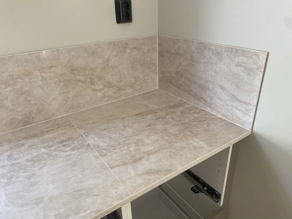 Hörn i kök med bänkskiva och stänkskydd i polerad Dekton Arga, ljus keramik med travertinlik ådring i Uddevalla.