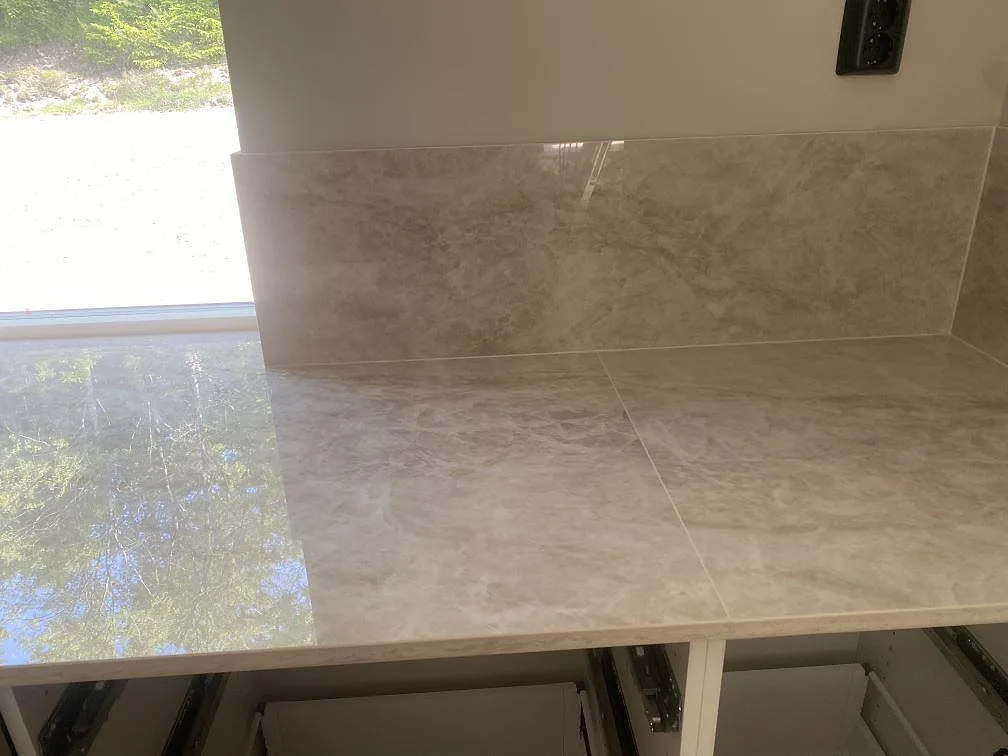Polerad Dekton Arga som köksbänkskiva under fönster, med 8 mm stänkskydd och ljus ådring i Uddevalla.