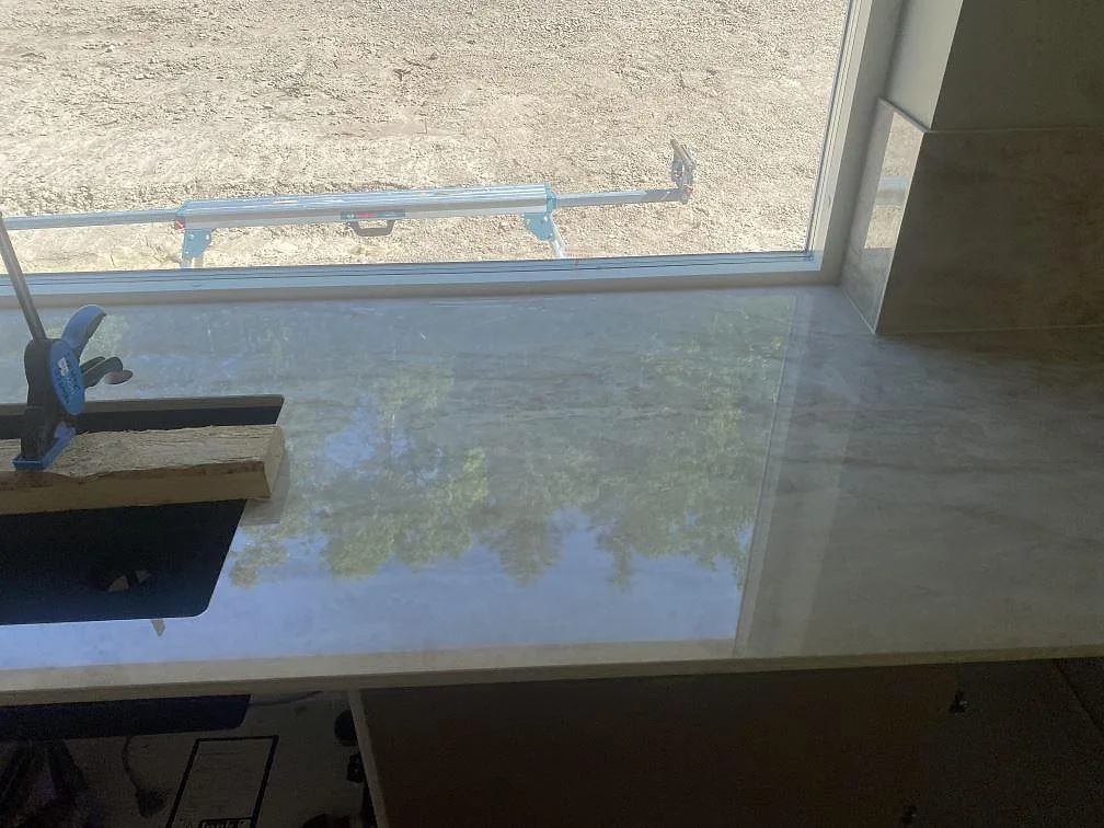 Köksbänkskiva i polerad Dekton Arga vid stort fönster, med svart underlimmad diskho under montering i Uddevalla.