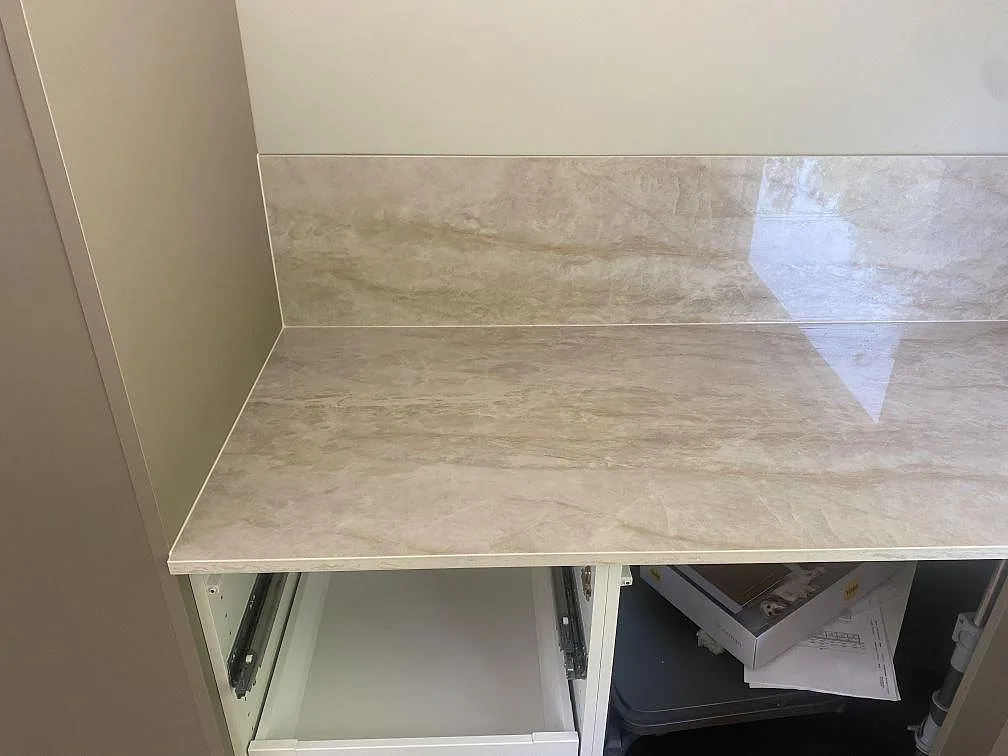 Närbild av polerad Dekton Arga som köksbänkskiva och matchande stänkskydd ovanför vita köksstommar i Uddevalla.