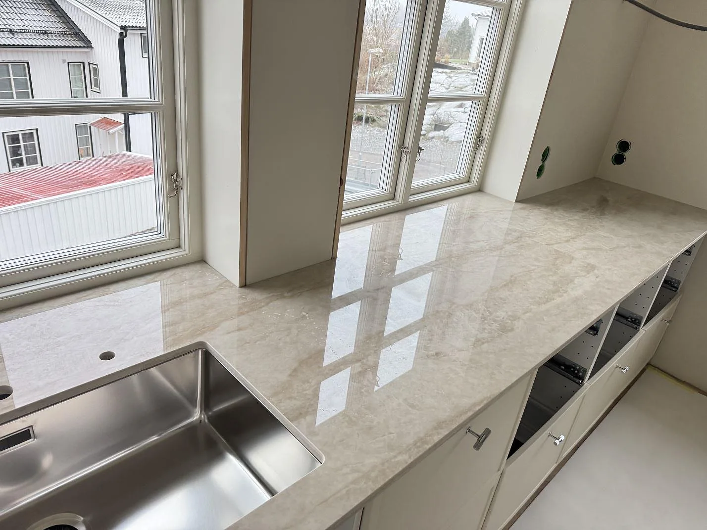 Köksbänkskiva i polerad Dekton Arga med rostfri diskho under fönstren i ett kök i Uddevalla.