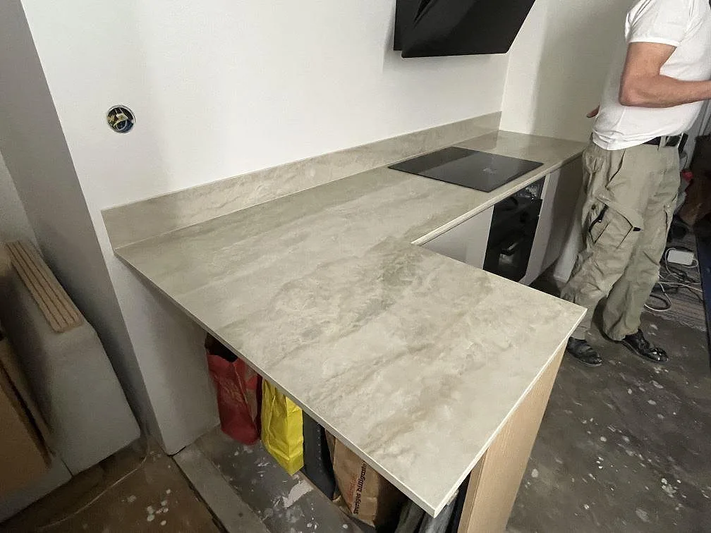 L-formad köksbänkskiva i polerad Dekton Arga med häll och lågt stänkskydd i ett kök under montering i Uppsala.