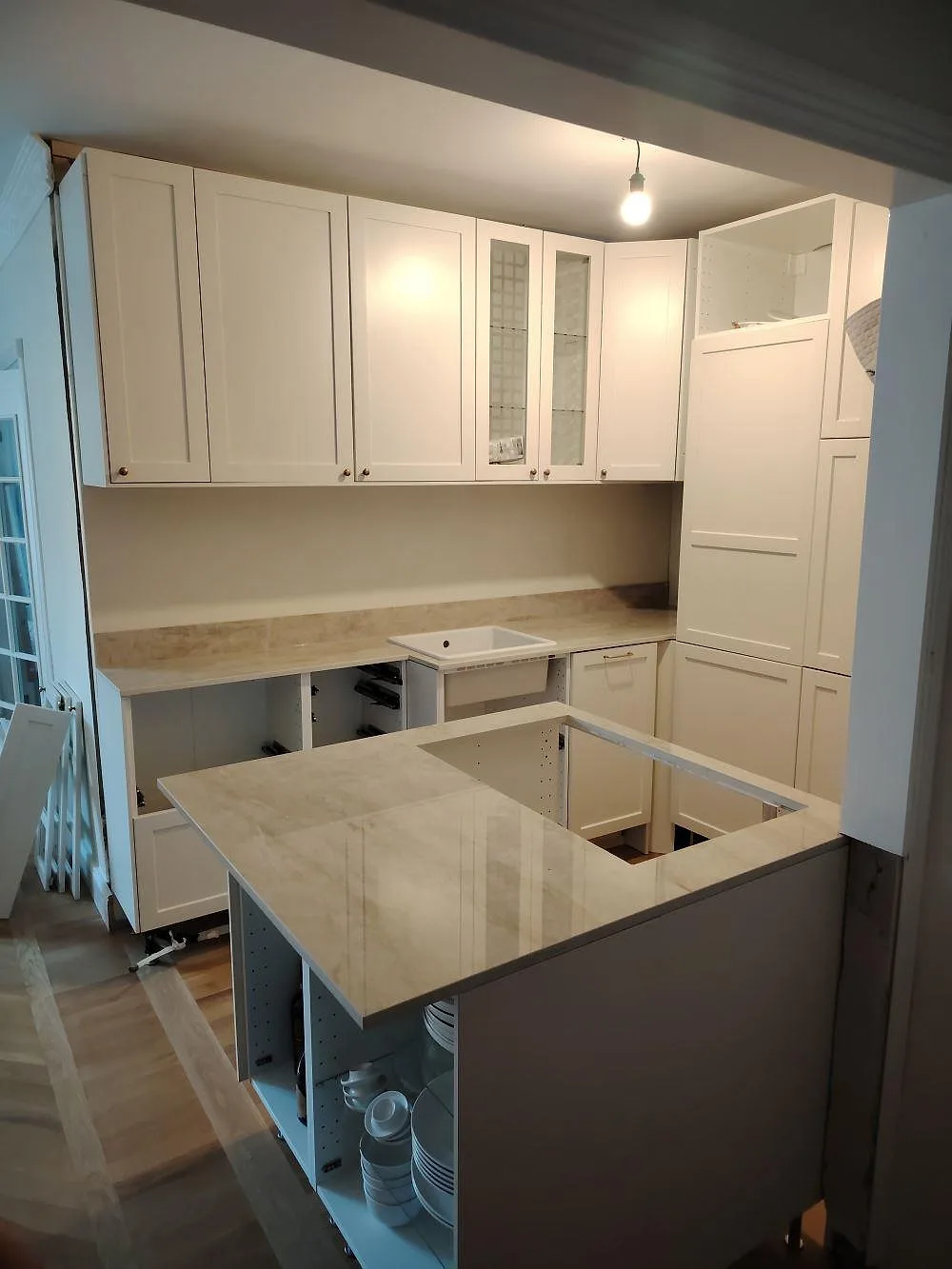 Polerad köksbänkskiva i Dekton Arga keramik med halvö, låg stänkkant och ljus ådring i ett vitt kök i Uppsala.