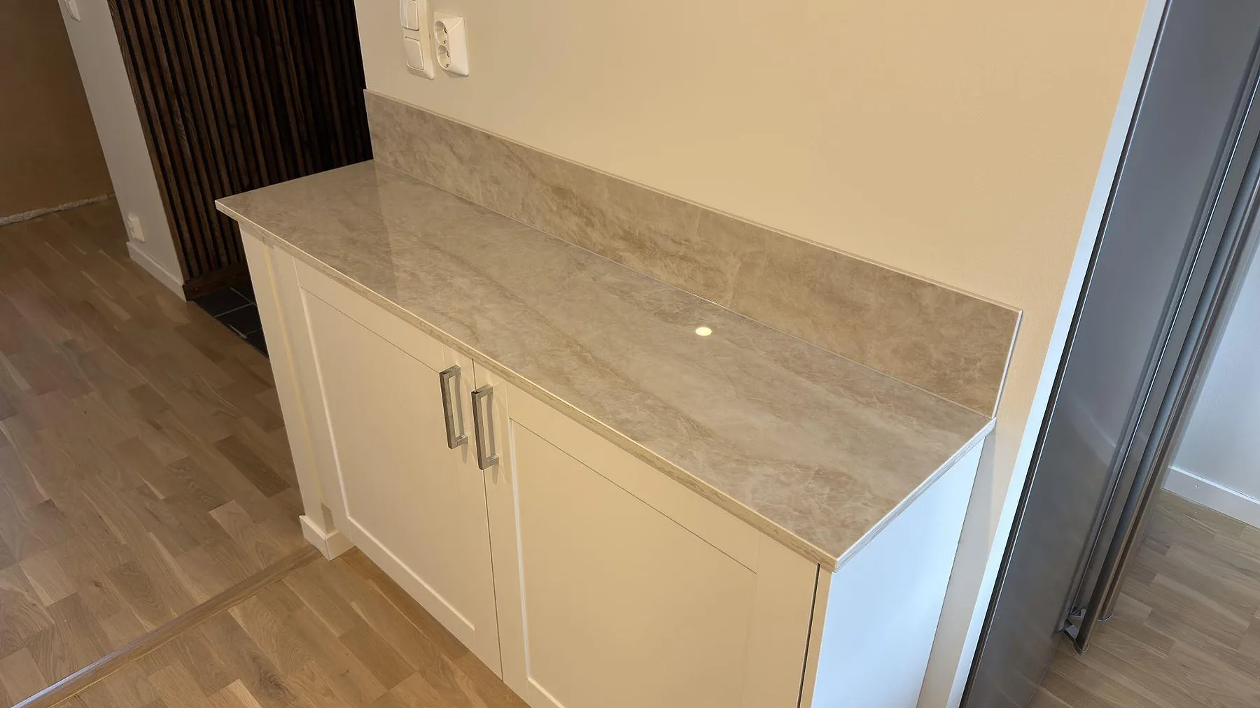 Sidobänk i polerad Dekton Arga med uppvikt stänkkant och ljus ådring i ett kök i Uppsala.