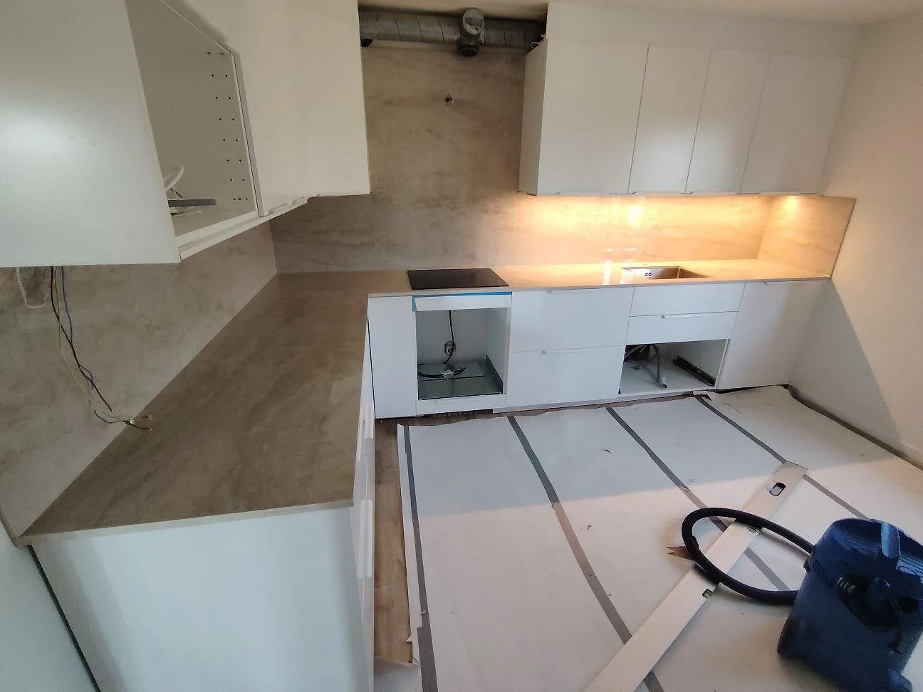 Köksbänkskiva i polerad Dekton Arga, beige keramik med matchande väggskivor och mjuk ådring, monterad i ett vitt kök under montering i Vällingby.