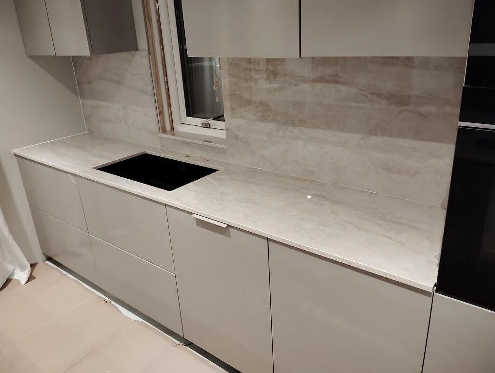 Bänkskiva och stänkskydd i polerad Dekton Arga längs köksvägg med ljusa skåp i Västerås.