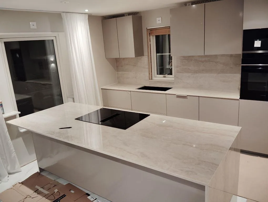 Köksbänkskiva i polerad Dekton Arga med köksö, häll och matchande stänkskydd i ett kök i Västerås.