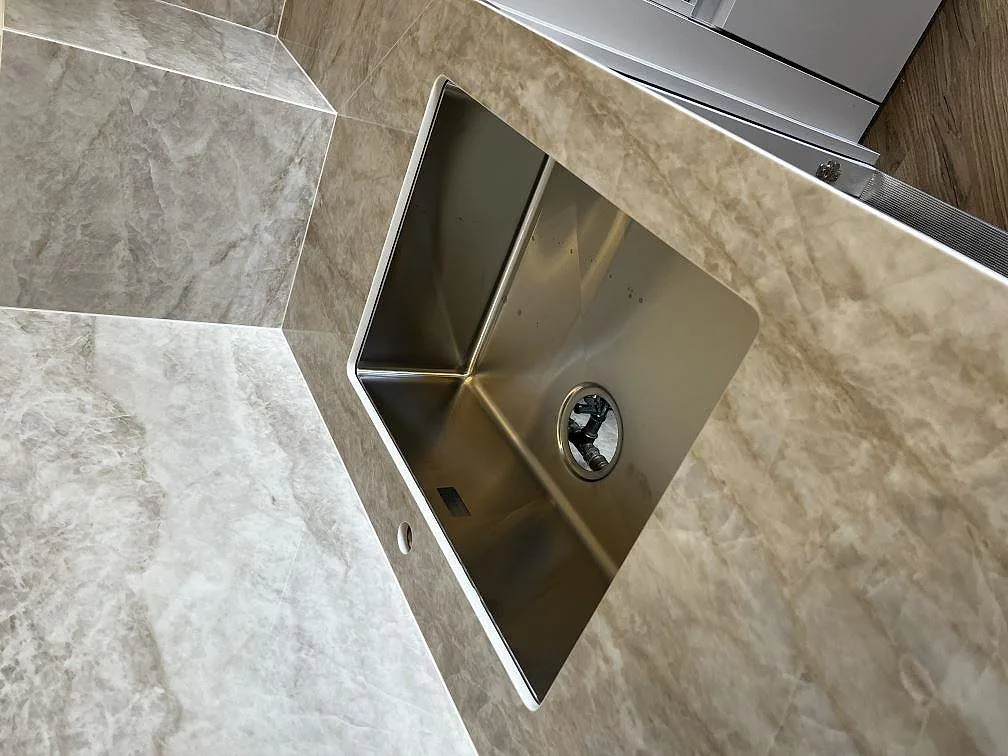 Underlimmad rostfri diskho i polerad Dekton Arga bänkskiva med mjuk brun-guldig ådring i ett kök i Valby.