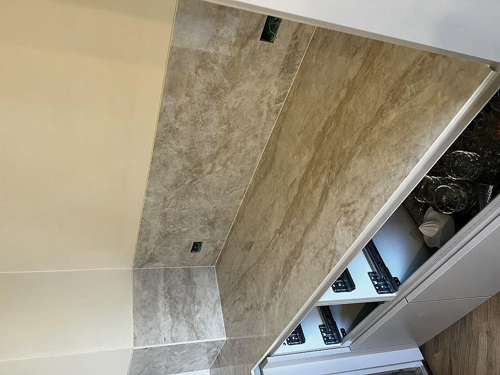 Uppvikt stänkskydd i polerad Dekton Arga med eluttag, krämvit marmorlik yta i ett kök i Valby.