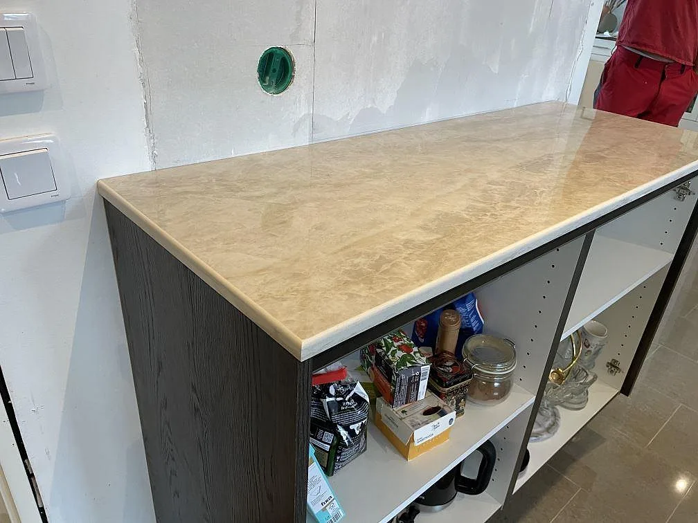 Rak bänkyta i polerad Dekton Arga, beige keramik över öppna köksstommar och mörk gavel i Veberöd.