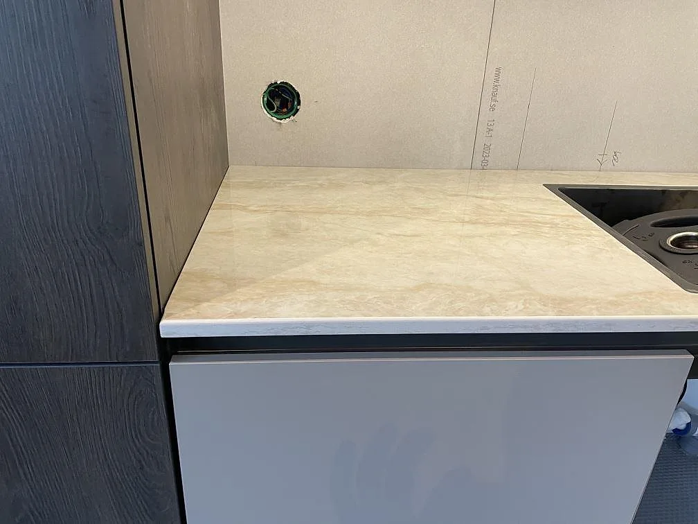 Detalj av polerad Dekton Arga köksbänkskiva med ljus beige ådring intill mörka skåp och diskho i Veberöd.