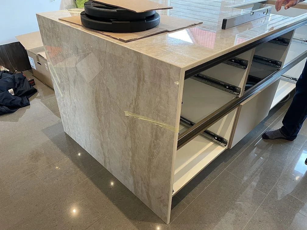 Köksö med bänkskiva och klädd gavel i polerad Dekton Arga, ljus keramik mot vita och mörka köksstommar i Veberöd.