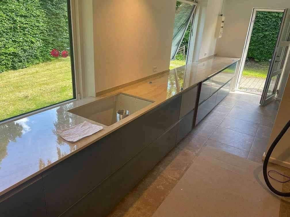 Polerad köksbänkskiva i Dekton Arga med låg stänkkant och diskbänkszon längs en fönstervägg i Vedbæk.