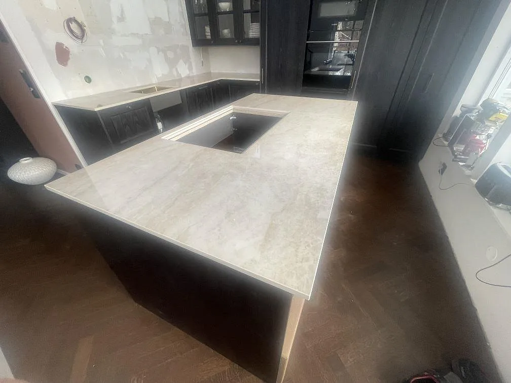 Köksbänkskiva och köksö i ljus polerad Dekton Arga, keramik, monterad i ett U-format kök med mörk inredning i Vendelsö.