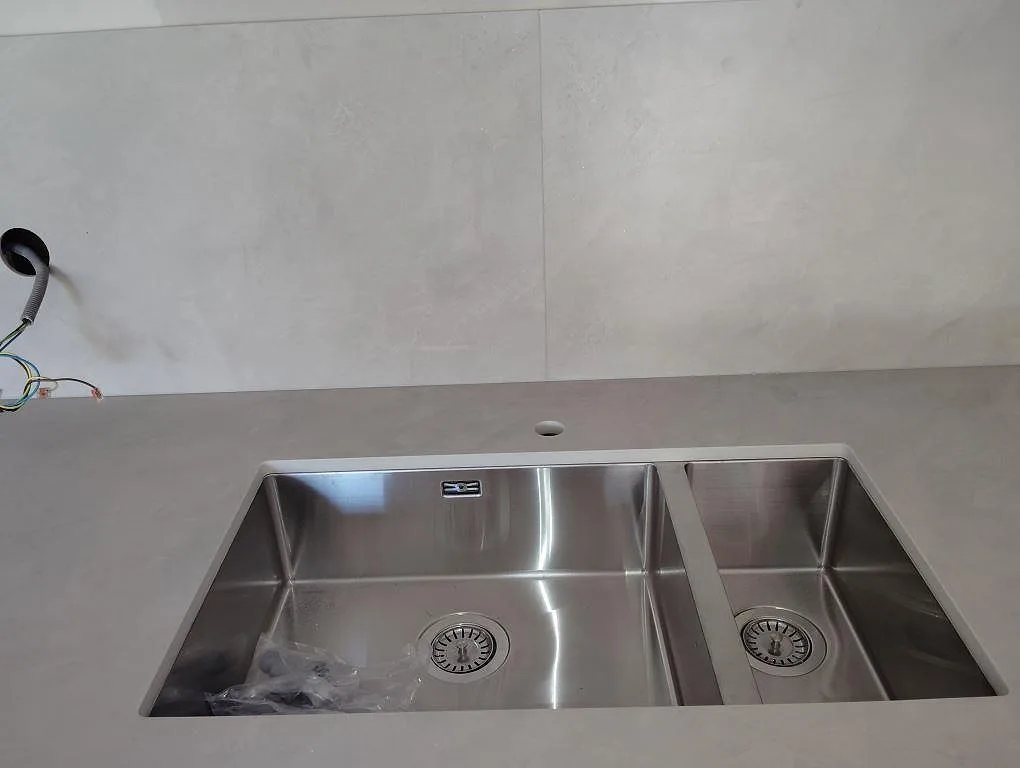 Närbild på grå matt Dekton Argentium med dubbel underlimmad rostfri diskho och matchande väggbeklädnad i Sollentuna.