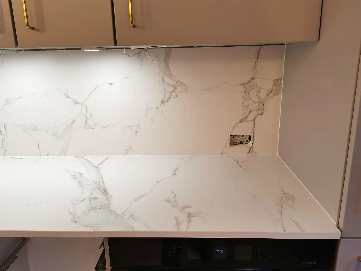 Matt vit Dekton Aura 15 bänkskiva med marmorlik ådring och stänkvägg ovanför inbyggnadsugnen i ett kök i Frederiksberg C.