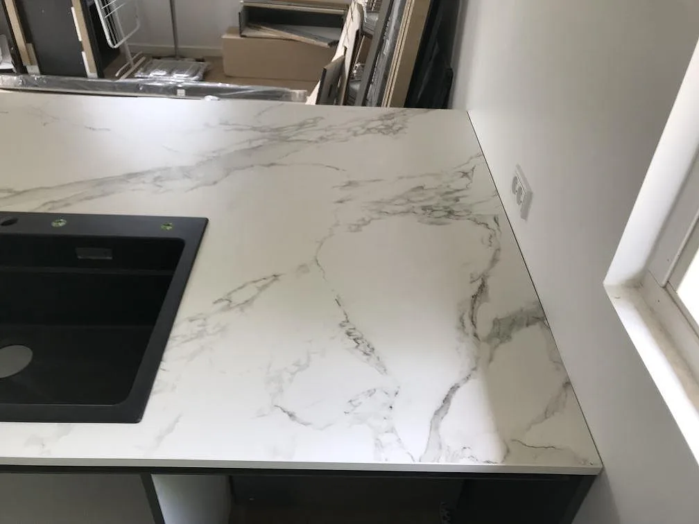 Hörn av köksbänkskiva i vit Dekton Aura 15, matt keramik, med svart kompositdiskho och tydlig grå ådring i ett kök i Ølstykke.