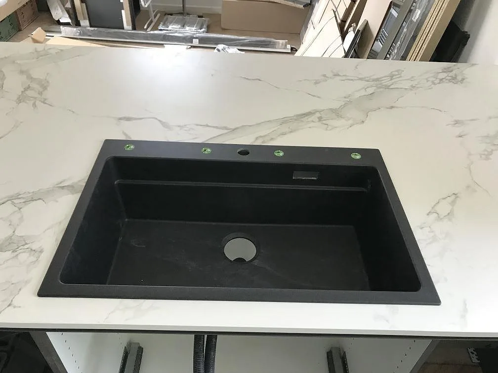 Svart kompositdiskho ovanpå köksbänkskiva i vit Dekton Aura 15 med borrade hål för köksblandare i ett kök i Ølstykke.