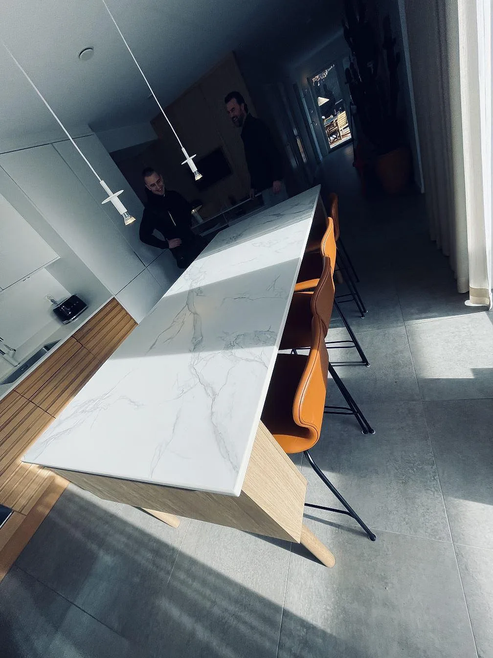 Vinklad vy längs köksön i Dekton Aura 22, matt keramik med kraftig grå ådring på vit botten, med cognacsfärgade barstolar i ett kök i Falkenberg.