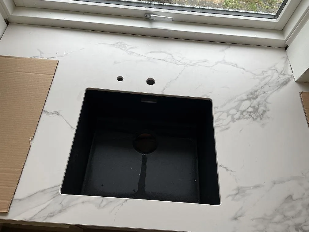 Närbild på svart diskho monterad under en matt Dekton Aura 22 bänkskiva med grå ådring i Glostrup.