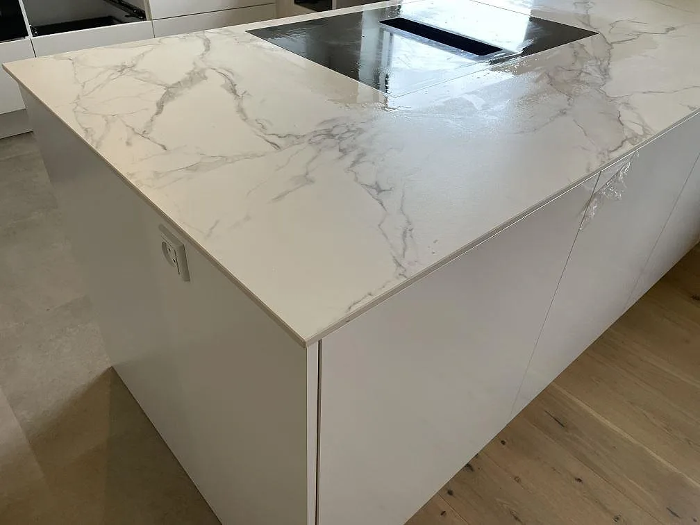 Halvö med köksbänkskiva i matt Dekton Aura 22 och infälld svart induktionshäll i ett vitt kök i Glostrup.