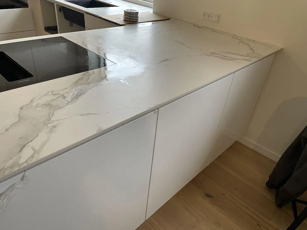 Vit Dekton Aura 22 bänkskiva i matt keramik med synlig grå ådring, häll och diskho under montering i Glostrup.