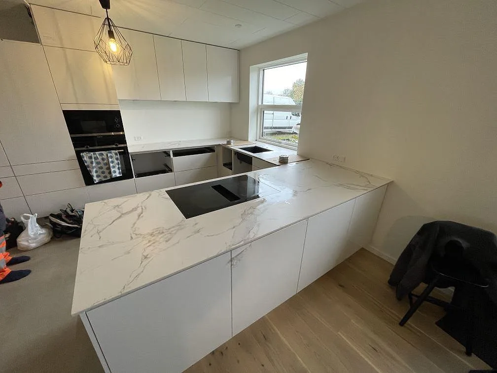 L-formad köksbänkskiva i matt Dekton Aura 22, vit keramik med grå ådring, svart diskho och induktionshäll i Glostrup.