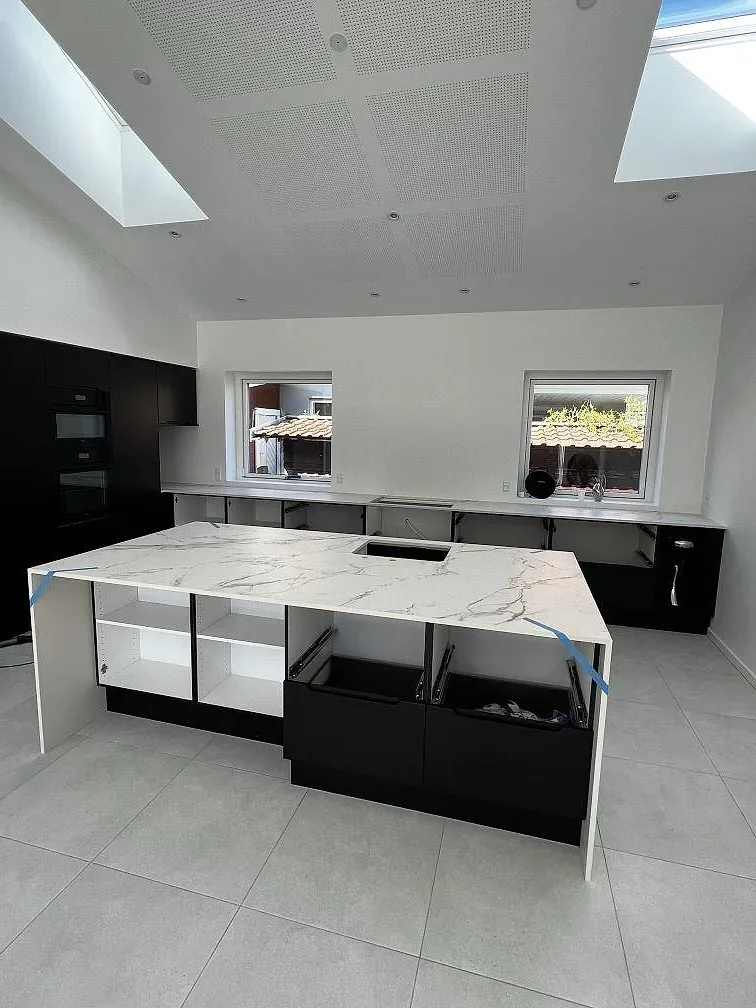 Köksö i vit Dekton Aura 22 under montering, med mörka stommar och grått klinkergolv i ett kök i Rødovre.