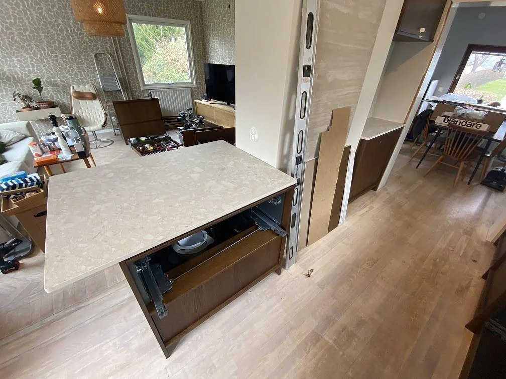 Köksö och sidobänk i matt Dekton Ava keramik med trästommar under montering i ett kök i Göteborg.
