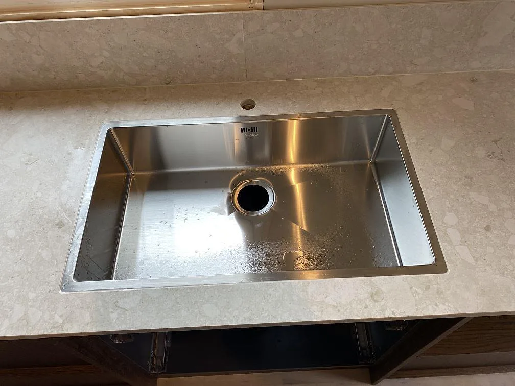 Rostfri diskho ovanpå en köksbänkskiva i matt Dekton Ava med matchande låg stänkkant i Göteborg.