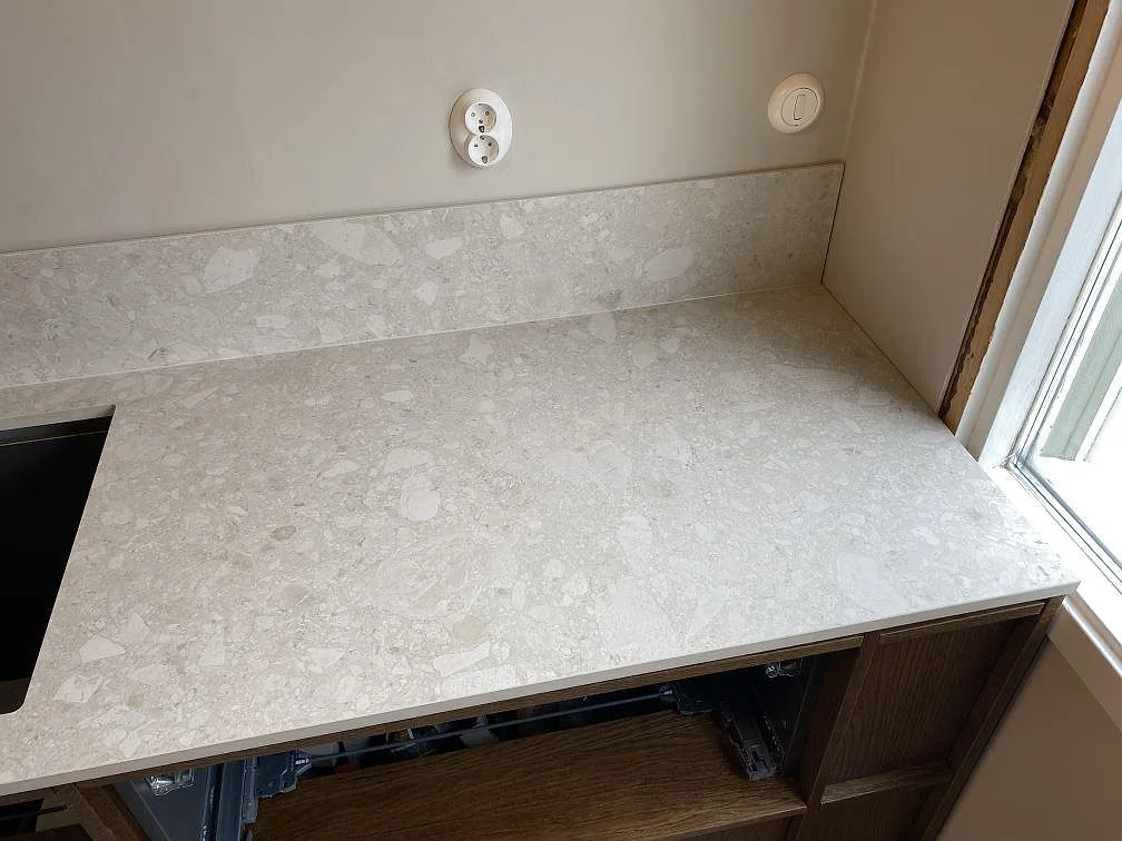 Höger bänkyta i matt Dekton Ava med låg stänkkant vid fönster och öppen trästomme i Göteborg.